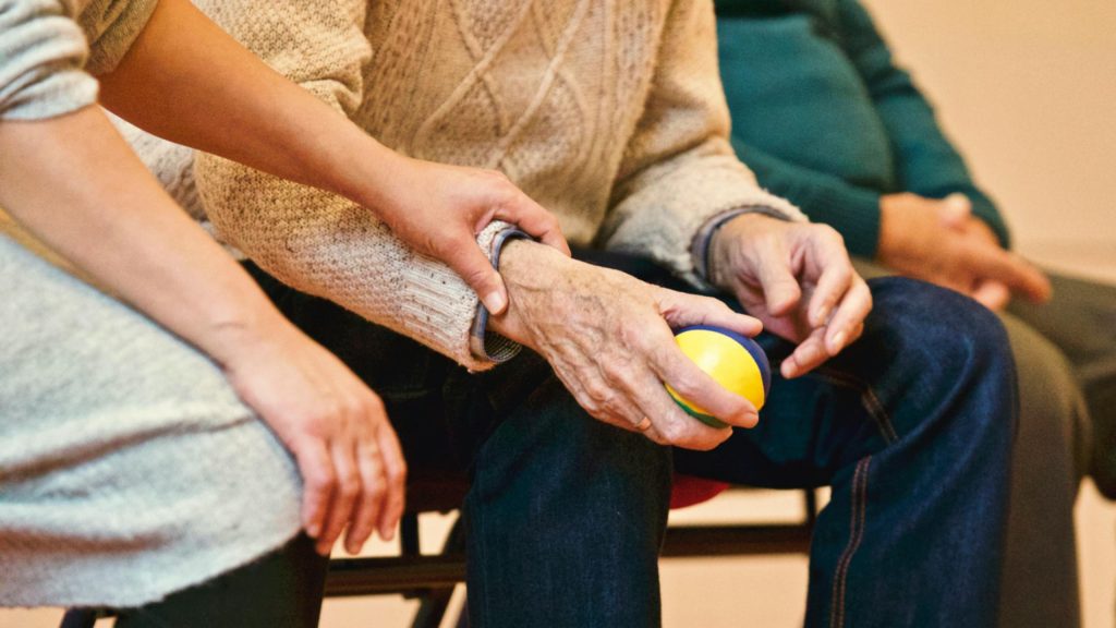 Badante aiuta un anziano con una pallina in mano